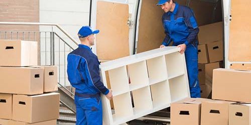 Movers Unloading Furniture From Truck. Young male movers unloading furniture and cardboard boxes from truck on street