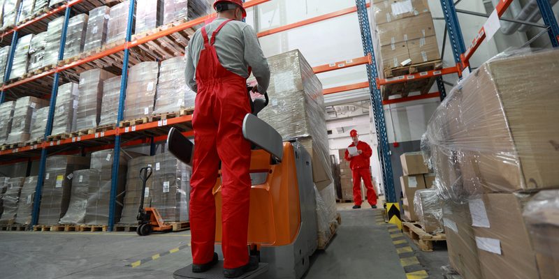 Goods delivery in storehouse. Goods delivery - two workers working in storehouse with forklift loader